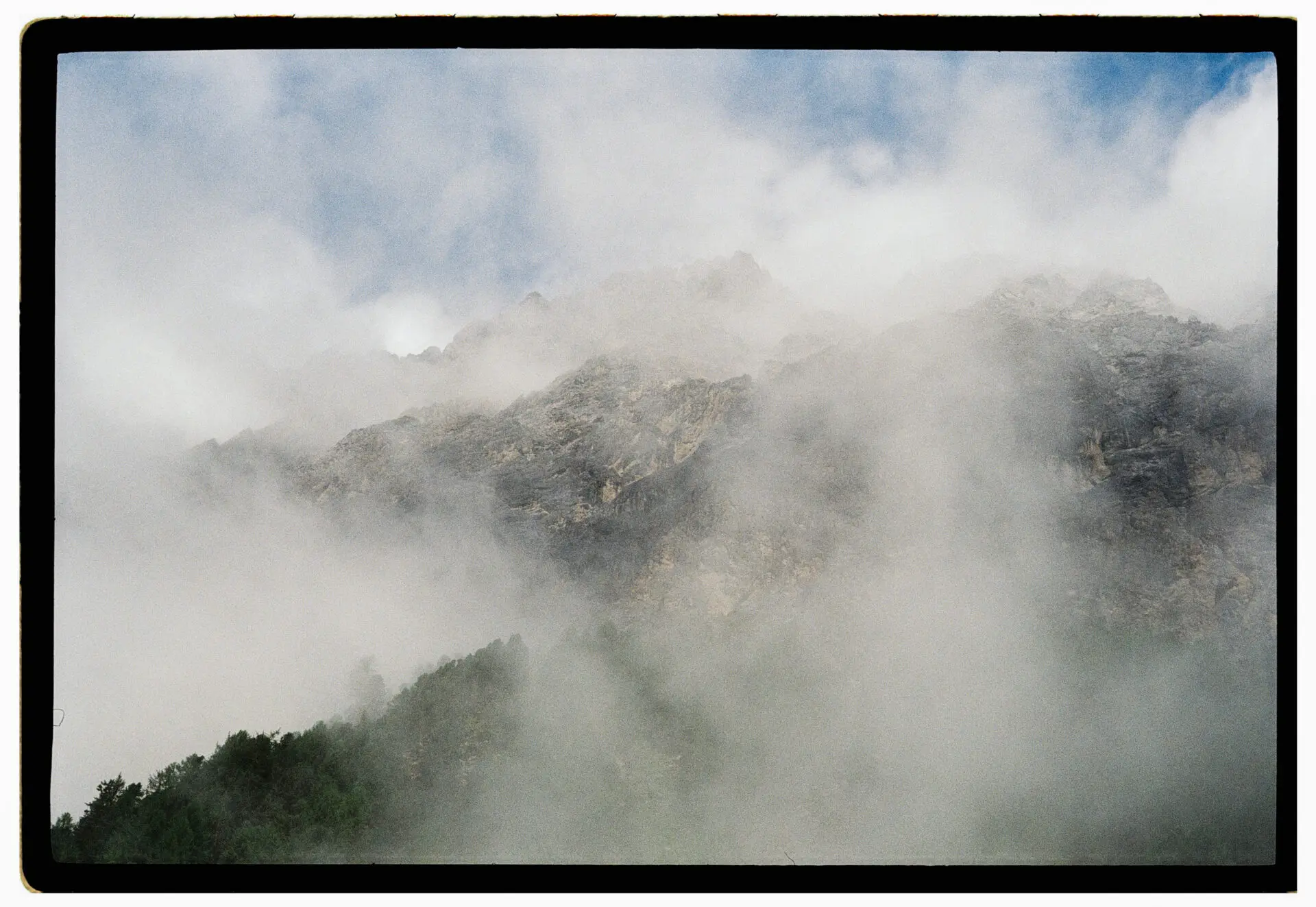Thick clouds moving over rugged mountain peaks, partially covering the landscape below.